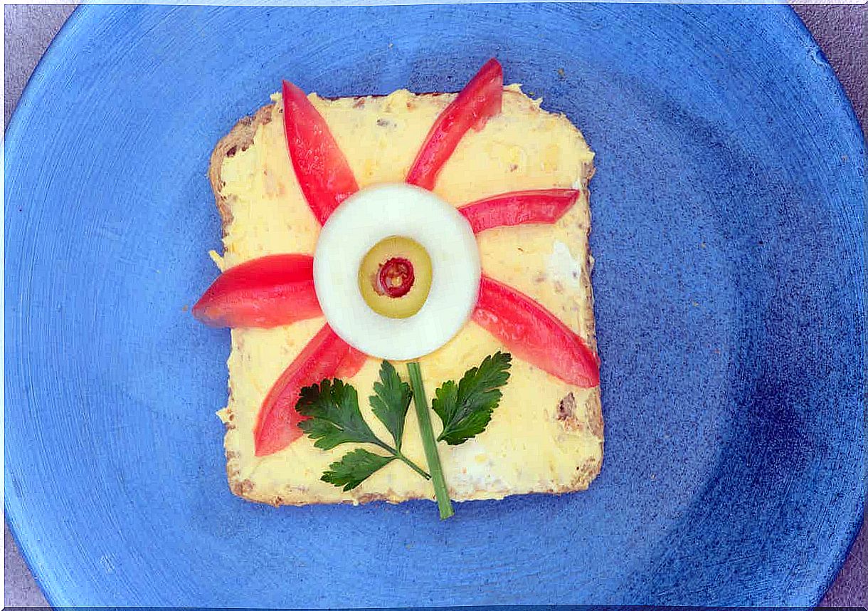 An egg sandwich with tomato wedges and an egg slice forming the shape of a flower.