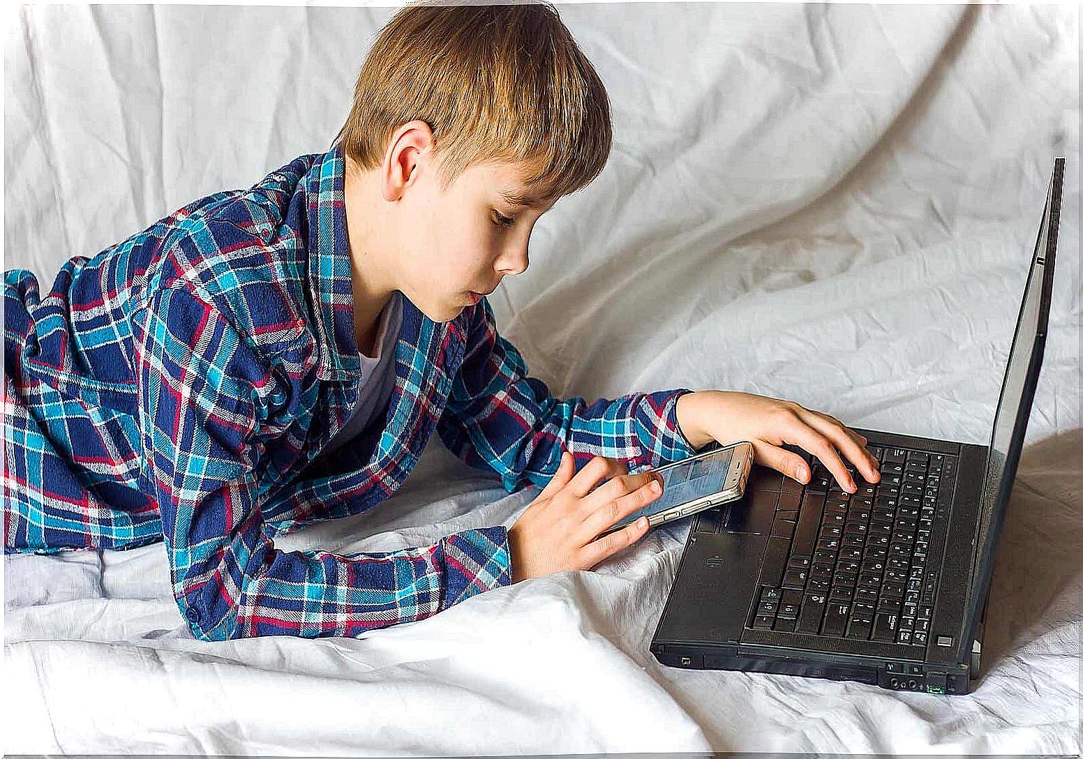 A teenager looking at his cell phone while working on the computer.