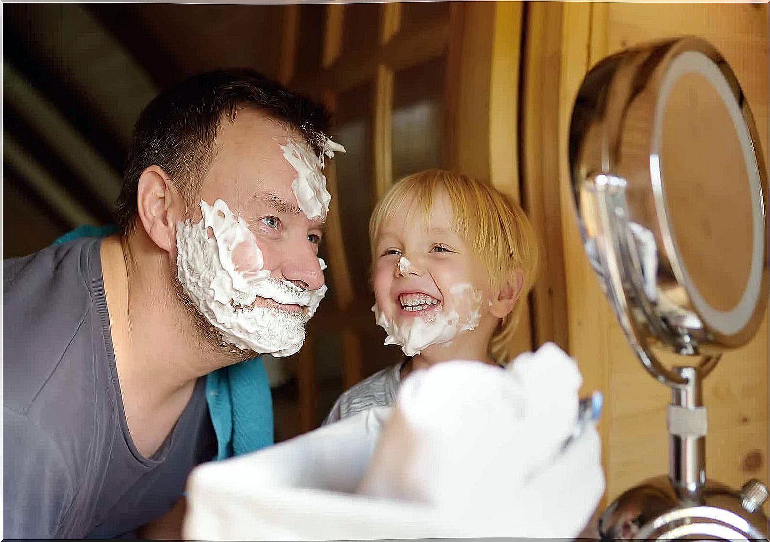 A father and son with shaving cream on their faces, smiling.