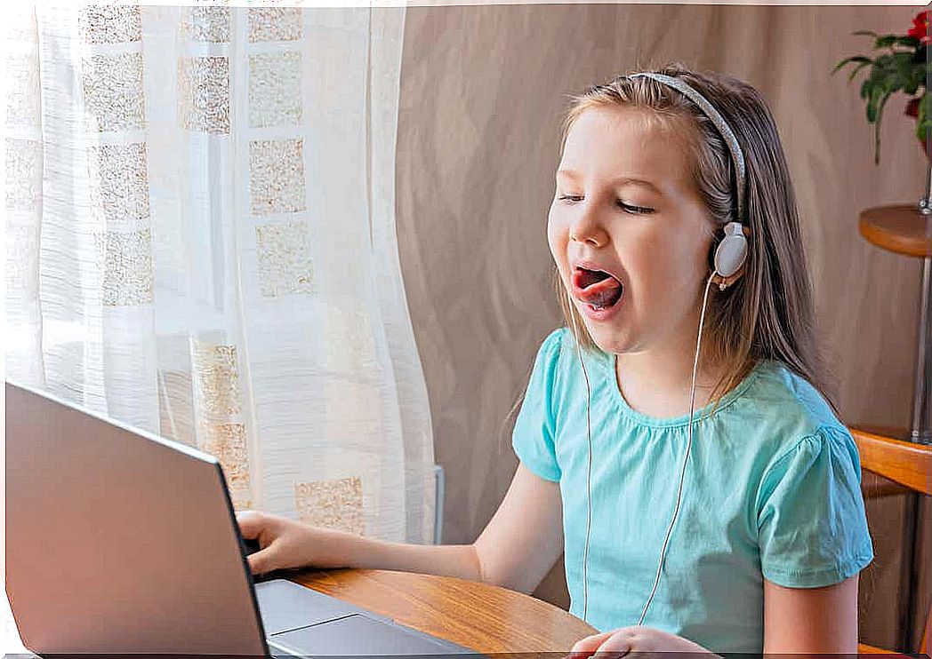 A young girl does tongue exercises during an online speech therapy session.