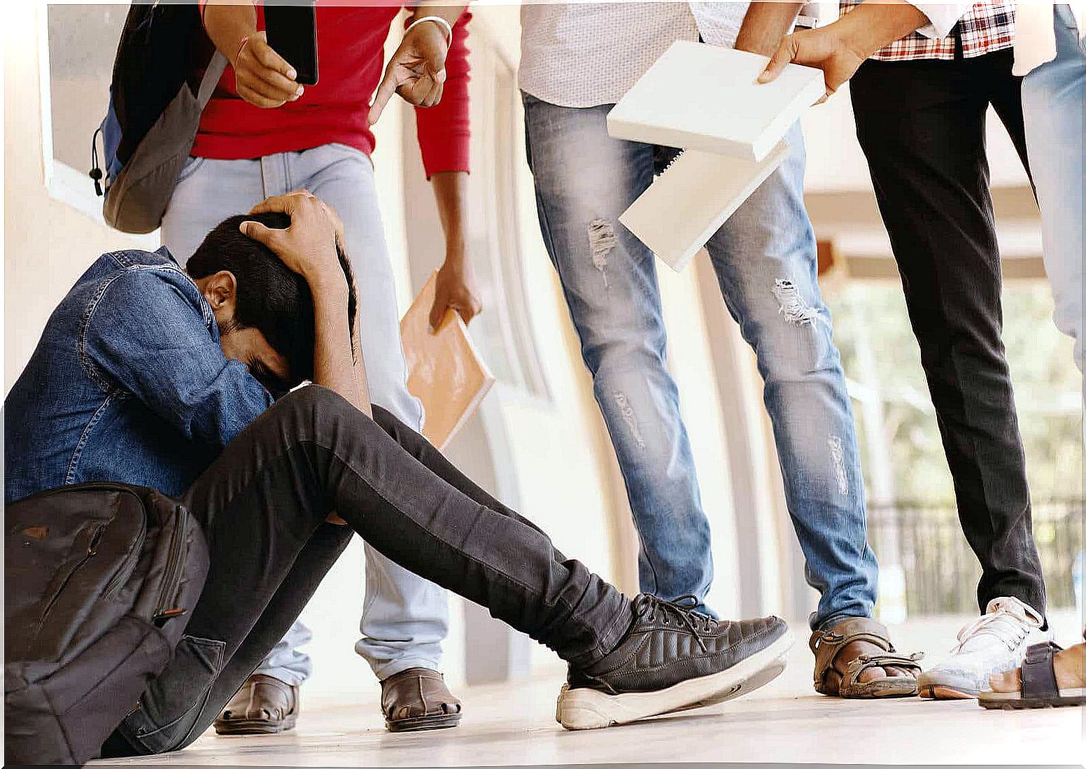 A teenage boy sitting on the floor at school, surrounded by a group of bullies.