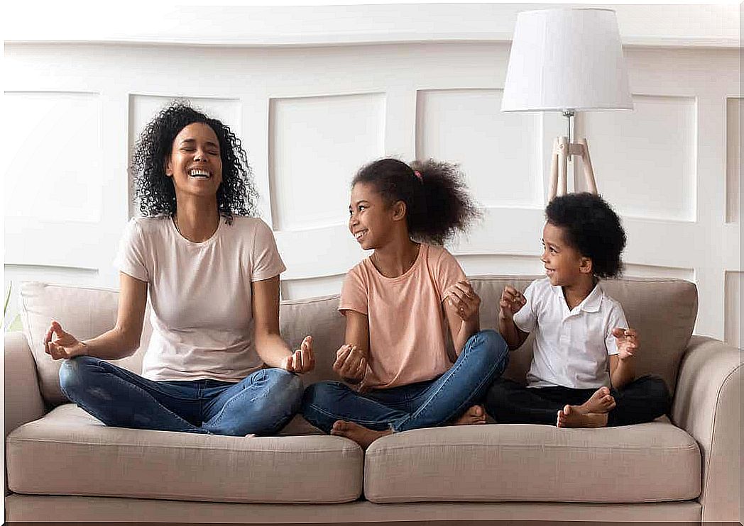 A mother meditating on the couch with her young daughter and son.